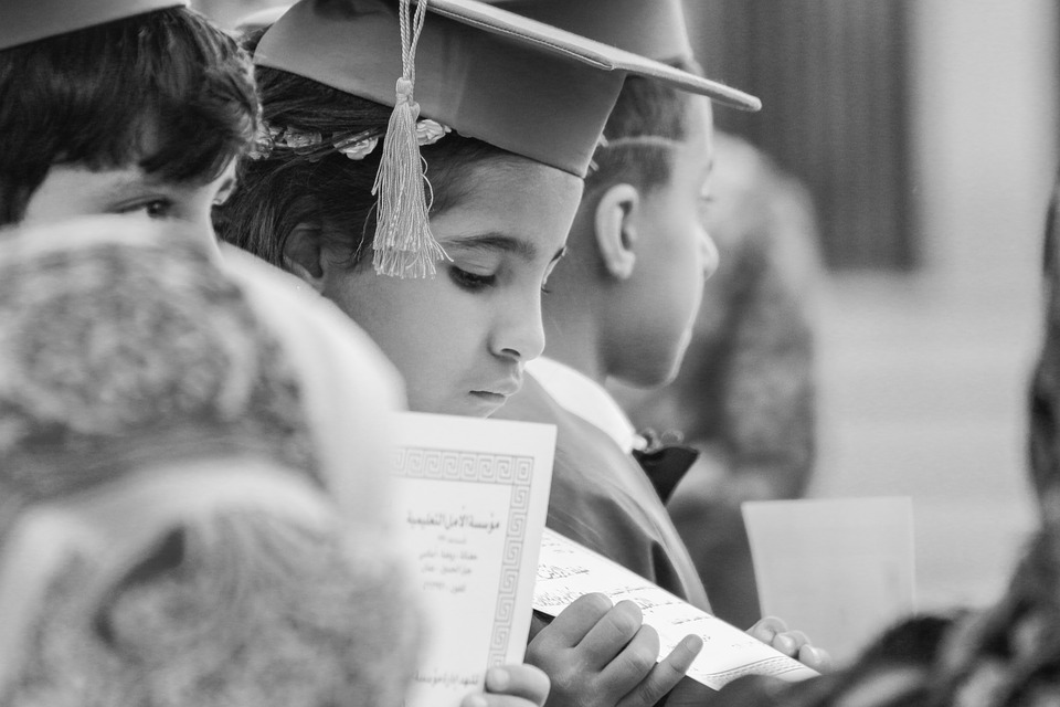 A Little Girl looks at her diploma with a cap and gown on